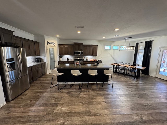 7001 La Escalera Ct, Odessa, TX 79765 - kitchen with appliances with stainless steel finishes, a kitchen bar, backsplash, dark brown cabinets, and an island with sink