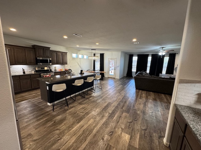 7001 La Escalera Ct, Odessa, TX 79765 - kitchen featuring stainless steel appliances, a kitchen breakfast bar, dark wood-style flooring, dark countertops, and open floor plan