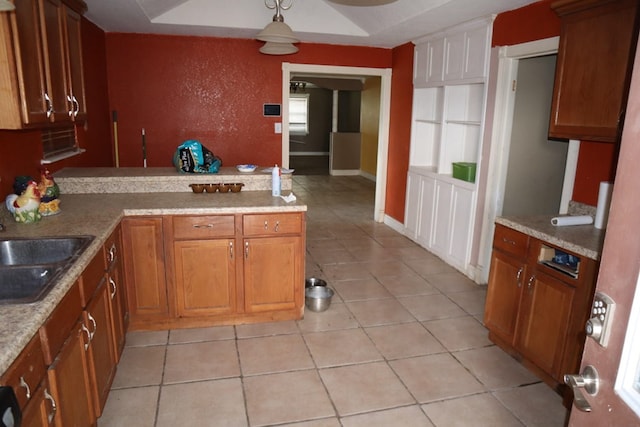 1642 S Plum Ave, Pecos, TX 79772 - kitchen featuring a sink, brown cabinetry, a peninsula, light countertops, and decorative light fixtures
