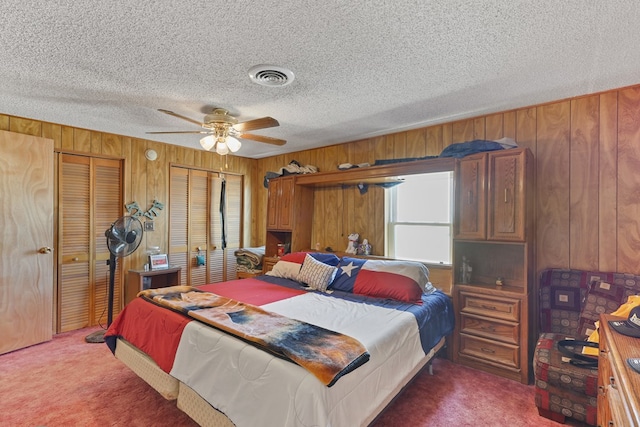 1908 W 36th St, Monahans, TX 79756 - bedroom with wood walls, carpet floors, two closets, a textured ceiling, and ceiling fan
