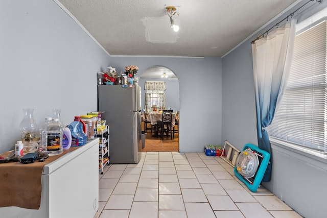 kitchen with light tile patterned floors, a textured ceiling, stainless steel refrigerator, and ornamental molding