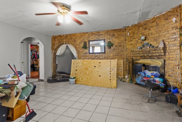 tiled living room with ceiling fan and brick wall