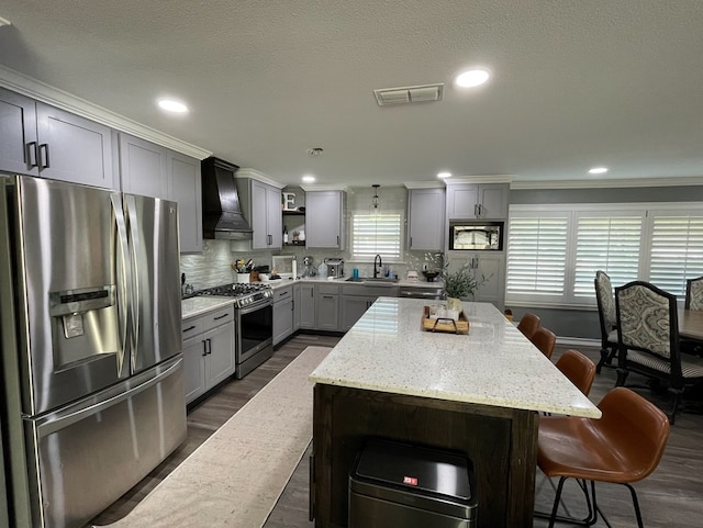 1401 S Franklin Ave, Monahans, TX 79756 - kitchen featuring stainless steel appliances, custom exhaust hood, gray cabinetry, a kitchen breakfast bar, and crown molding