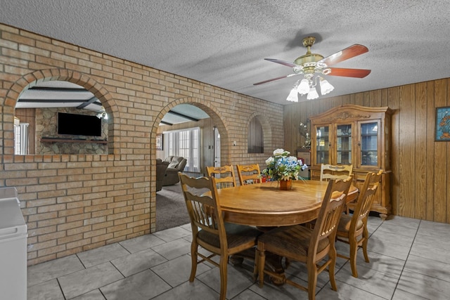 tiled dining area with wood walls, brick wall, ceiling fan, a textured ceiling, and arched walkways