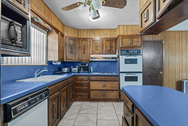 kitchen featuring white appliances, a sink, dark countertops, a textured ceiling, and wood walls