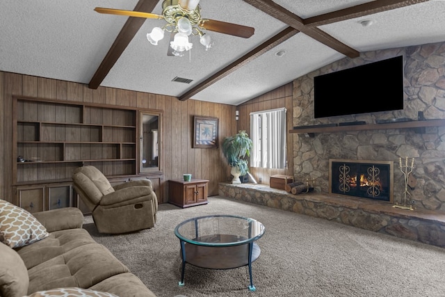 carpeted living area featuring a textured ceiling, wood walls, ceiling fan, and a stone fireplace