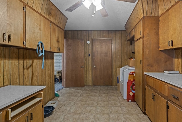 laundry room with washer and clothes dryer, wooden walls, ceiling fan, a textured ceiling, and stone finish floors
