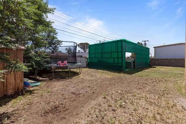 view of outbuilding with a trampoline, fence, and an outbuilding