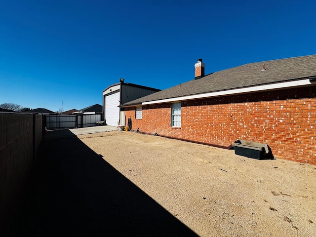 view of property exterior with fence, driveway, a chimney, an outdoor structure, and brick siding