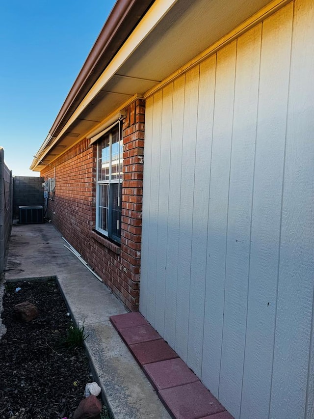 view of side of property featuring cooling unit, brick siding, and fence