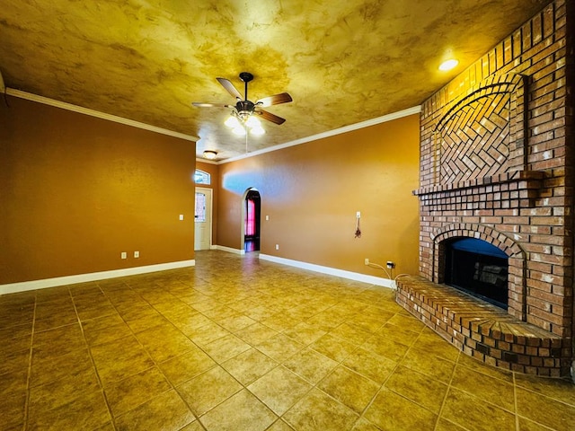 unfurnished living room with tile patterned flooring, a brick fireplace, baseboards, ornamental molding, and a ceiling fan