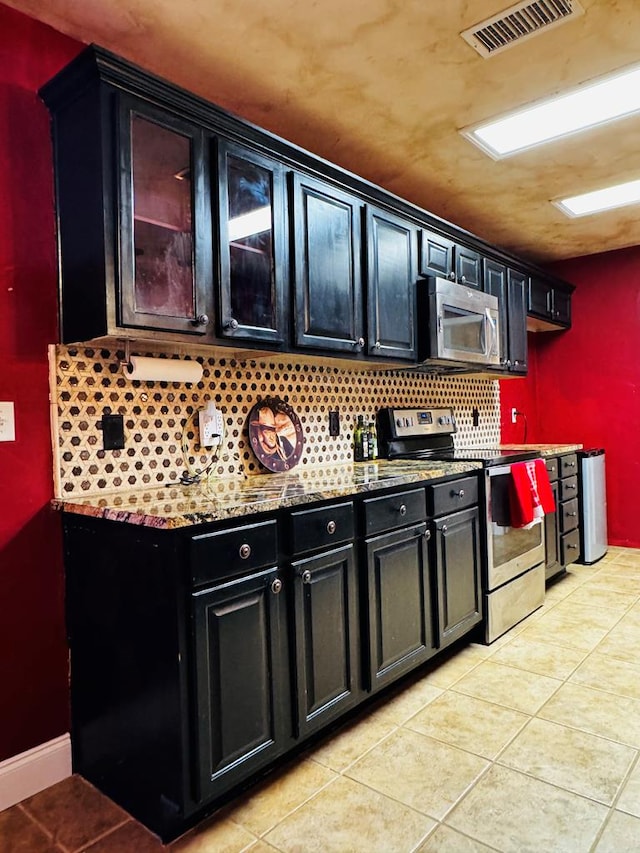 kitchen featuring light tile patterned floors, visible vents, appliances with stainless steel finishes, dark cabinets, and backsplash