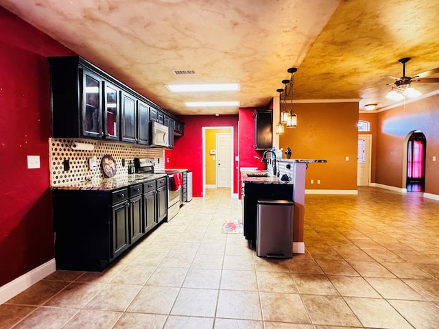 kitchen with a sink, dark cabinetry, appliances with stainless steel finishes, baseboards, and light stone countertops