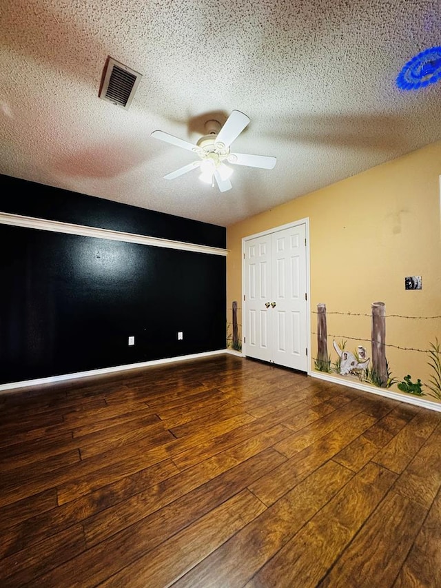 empty room with hardwood / wood-style flooring, a ceiling fan, visible vents, and a textured ceiling