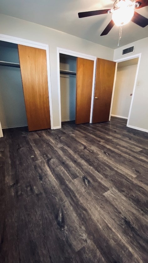 unfurnished bedroom with dark wood-type flooring, multiple closets, ceiling fan, and baseboards