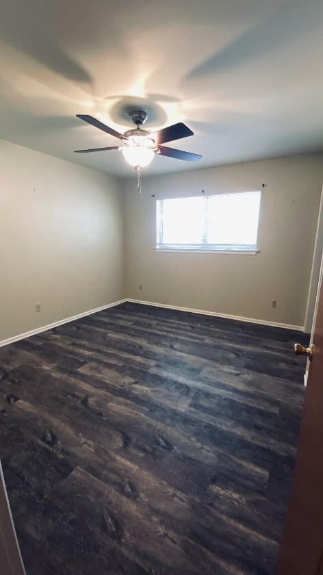 empty room with baseboards, dark wood-style floors, and ceiling fan