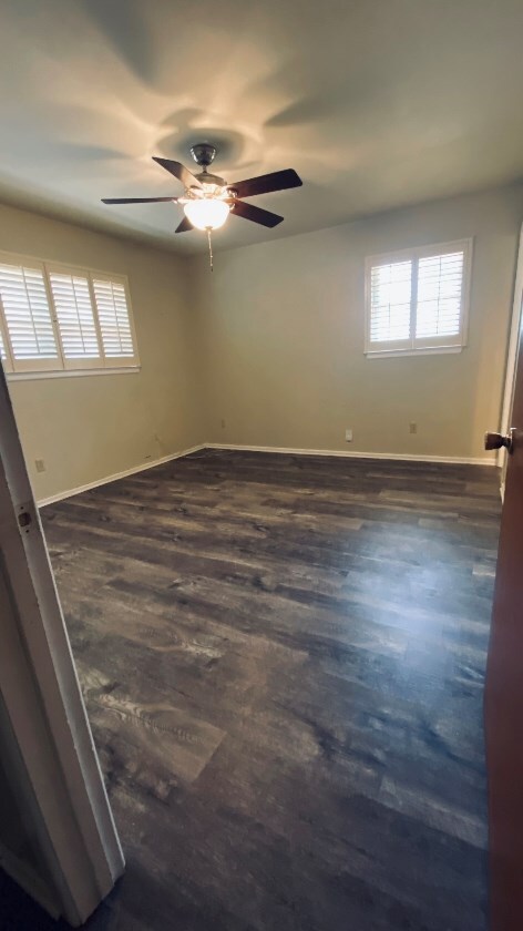 empty room with baseboards, ceiling fan, and dark wood-type flooring
