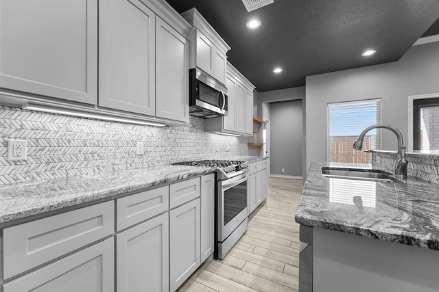 kitchen with light wood-style flooring, a sink, stainless steel appliances, light stone countertops, and tasteful backsplash