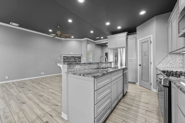 kitchen featuring a ceiling fan, appliances with stainless steel finishes, light wood finished floors, a sink, and an island with sink