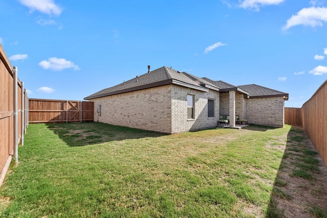 rear view of property with a yard, brick siding, and a fenced backyard