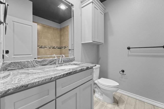full bathroom with toilet, wood finished floors, vanity, a textured wall, and baseboards