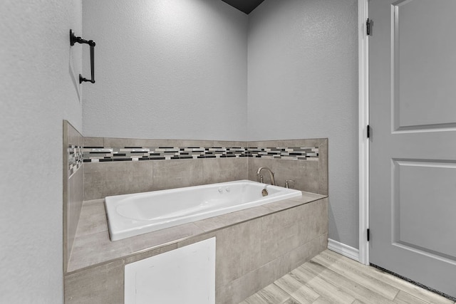 full bathroom featuring baseboards, a garden tub, a textured wall, and wood finished floors