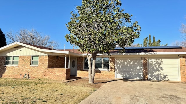 ranch-style home with a garage, a front yard, and solar panels