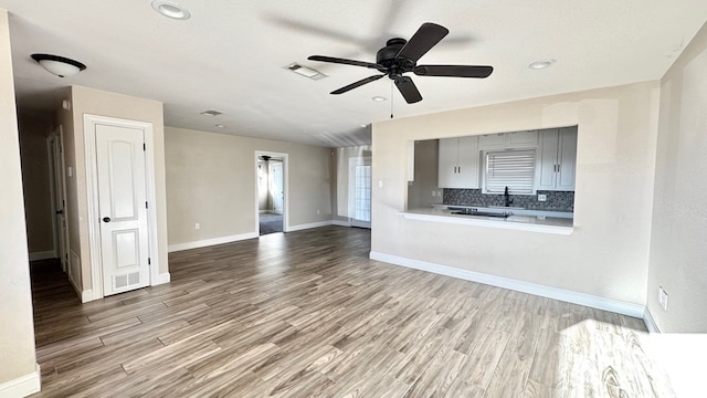 unfurnished living room with sink, a textured ceiling, wood-type flooring, and ceiling fan