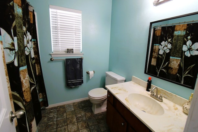 full bath featuring toilet, stone finish floors, vanity, baseboards, and a shower with shower curtain