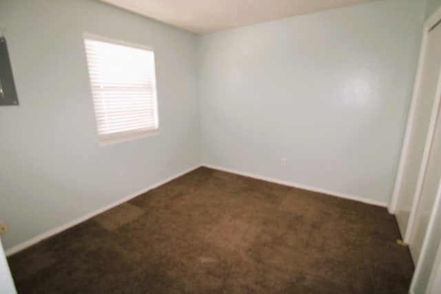 unfurnished room featuring dark colored carpet and baseboards