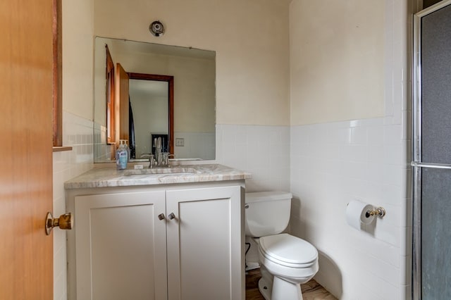 bathroom featuring toilet, an enclosed shower, vanity, and tile walls