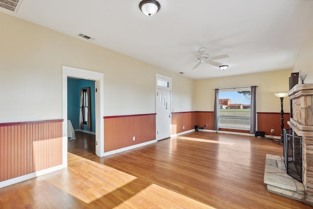 101 N 7th St, Marathon, TX 79842 - unfurnished living room with wood finished floors, a wainscoted wall, a ceiling fan, a stone fireplace, and baseboards