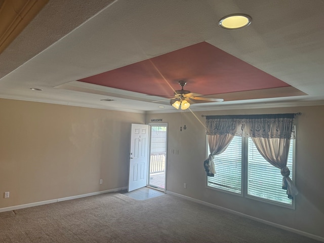 carpeted spare room with ceiling fan, visible vents, a raised ceiling, baseboards, and ornamental molding
