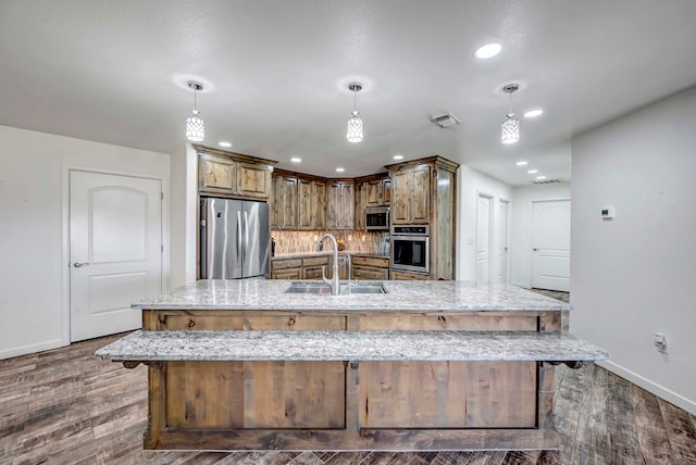 kitchen featuring stainless steel appliances, sink, a large island with sink, and decorative light fixtures