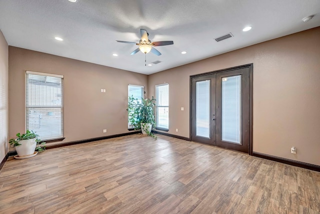 empty room featuring a textured ceiling, light hardwood / wood-style flooring, french doors, and ceiling fan