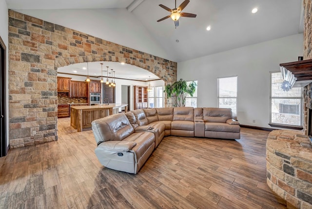 living room featuring ceiling fan with notable chandelier, a wealth of natural light, high vaulted ceiling, and light wood-type flooring