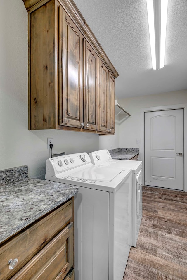 washroom with cabinets, light hardwood / wood-style floors, washer and dryer, and a textured ceiling