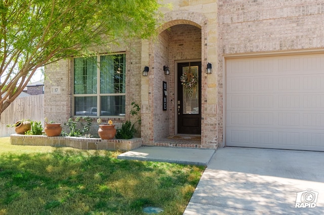 view of exterior entry with fence, driveway, stone siding, brick siding, and a yard