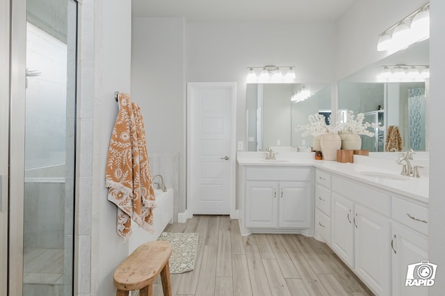 bathroom featuring a garden tub, double vanity, a shower with door, wood finished floors, and a sink