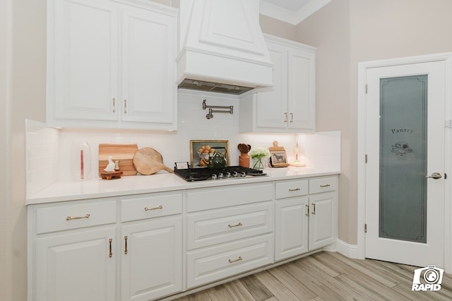 bar with light wood finished floors, stainless steel gas stovetop, premium range hood, and tasteful backsplash