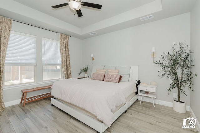 bedroom with baseboards, a tray ceiling, light wood-type flooring, and visible vents