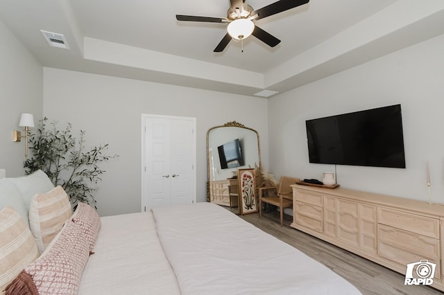 bedroom featuring a ceiling fan, visible vents, wood finished floors, and a raised ceiling