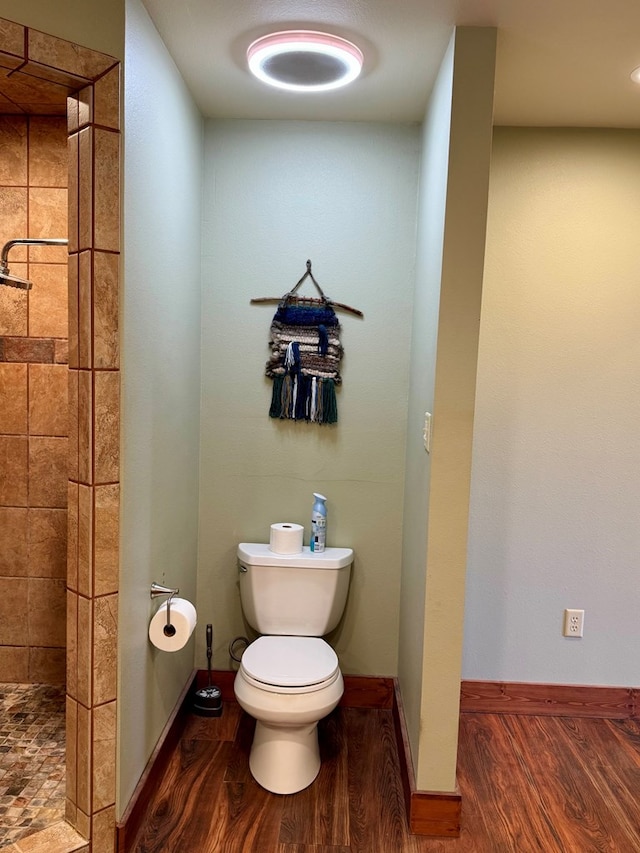 bathroom with hardwood / wood-style flooring, toilet, and tiled shower