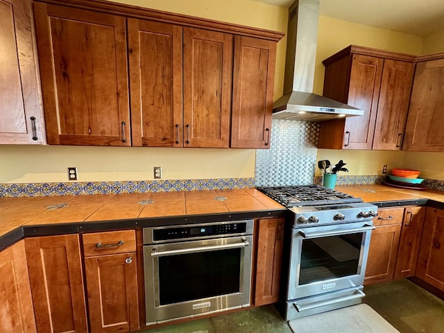 kitchen featuring appliances with stainless steel finishes, tile counters, decorative backsplash, and wall chimney exhaust hood