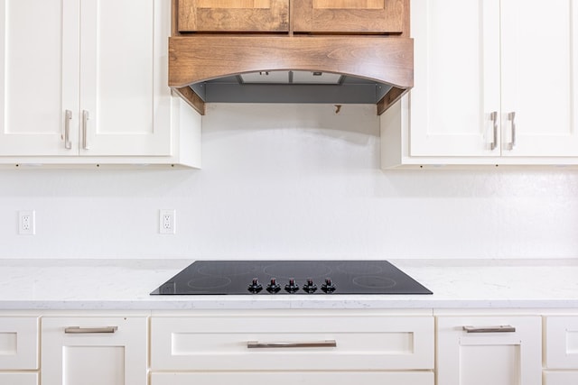 479 County Rd 306, Seminole, TX 79360 - kitchen with black electric cooktop, range hood, white cabinetry, and light stone countertops