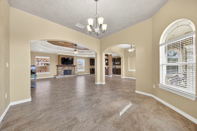 14 Da Vinci Ct, Odessa, TX 79765 - unfurnished living room featuring a stone fireplace, arched walkways, a ceiling fan, baseboards, and a textured ceiling