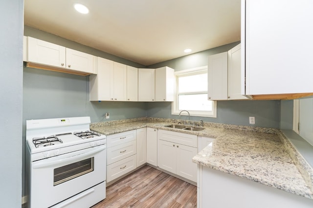kitchen with a sink, white gas stove, and white cabinetry