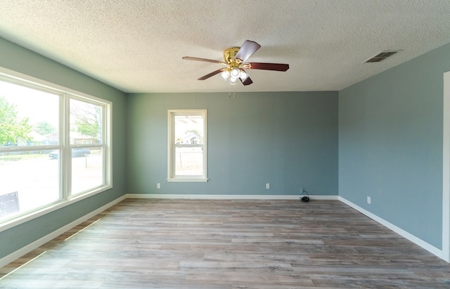spare room featuring a textured ceiling, ceiling fan, wood finished floors, and visible vents