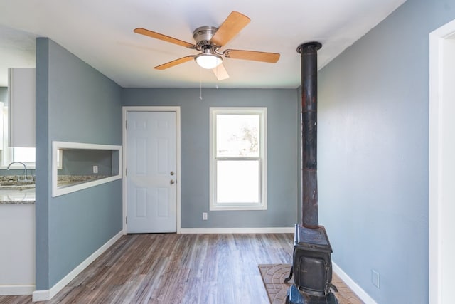 entryway featuring baseboards, a ceiling fan, a wood stove, and wood finished floors