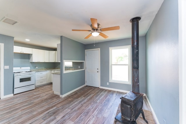 kitchen featuring visible vents, a wood stove, baseboards, white range with gas stovetop, and white cabinets